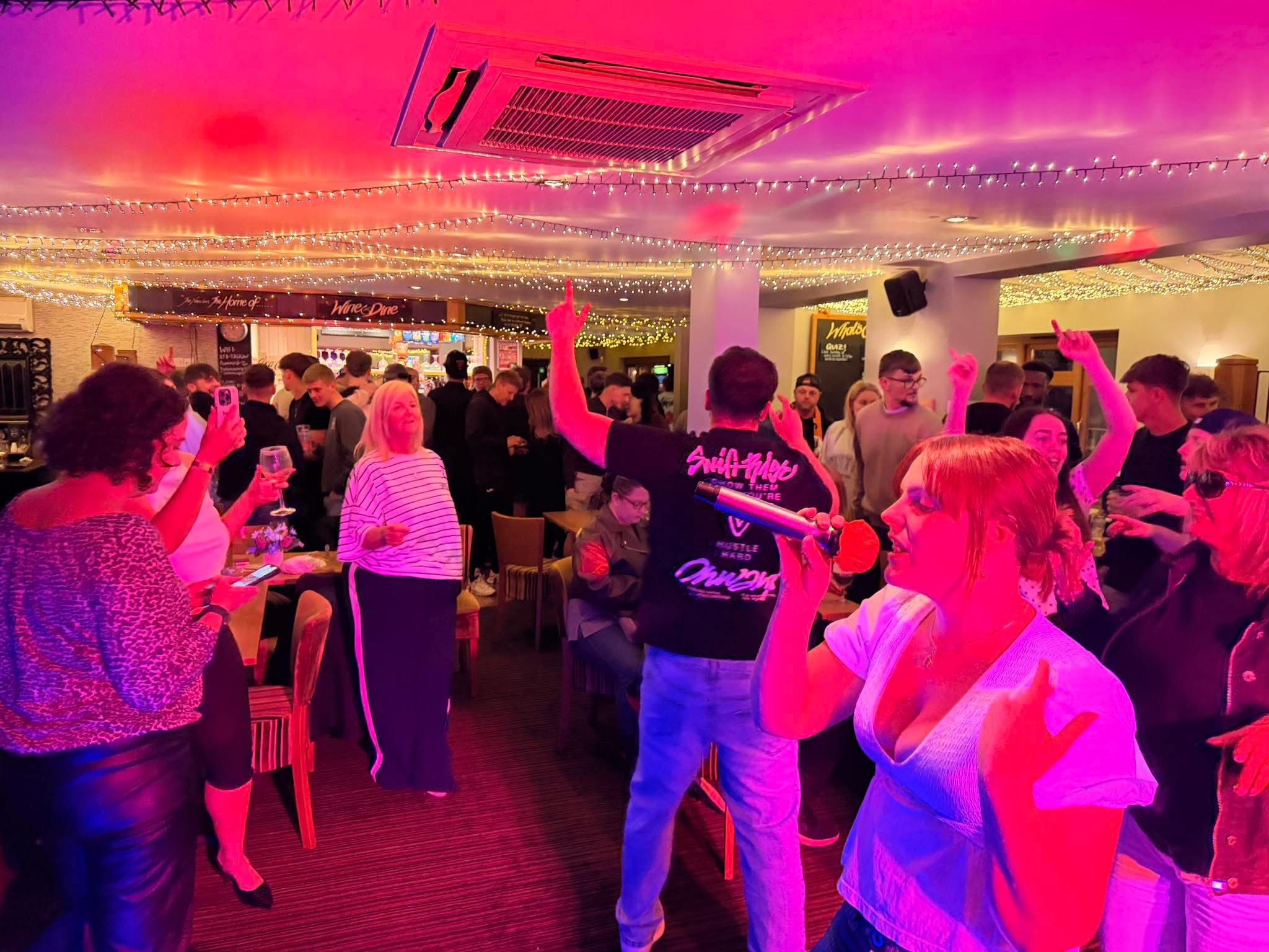 A guest singing into a microphone during a busy karaoke night.