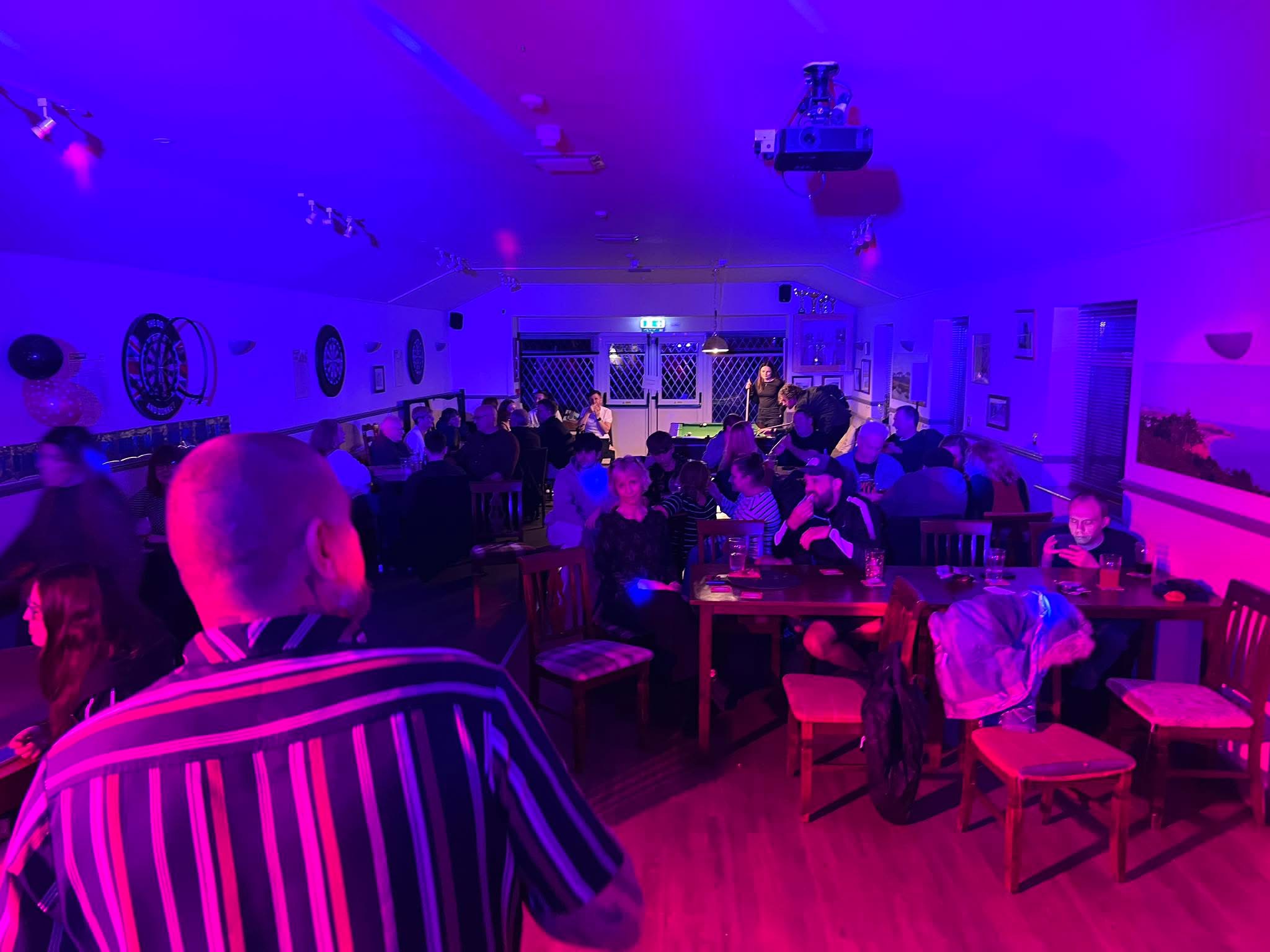 Guests enjoying a karaoke night under purple and pink lighting.