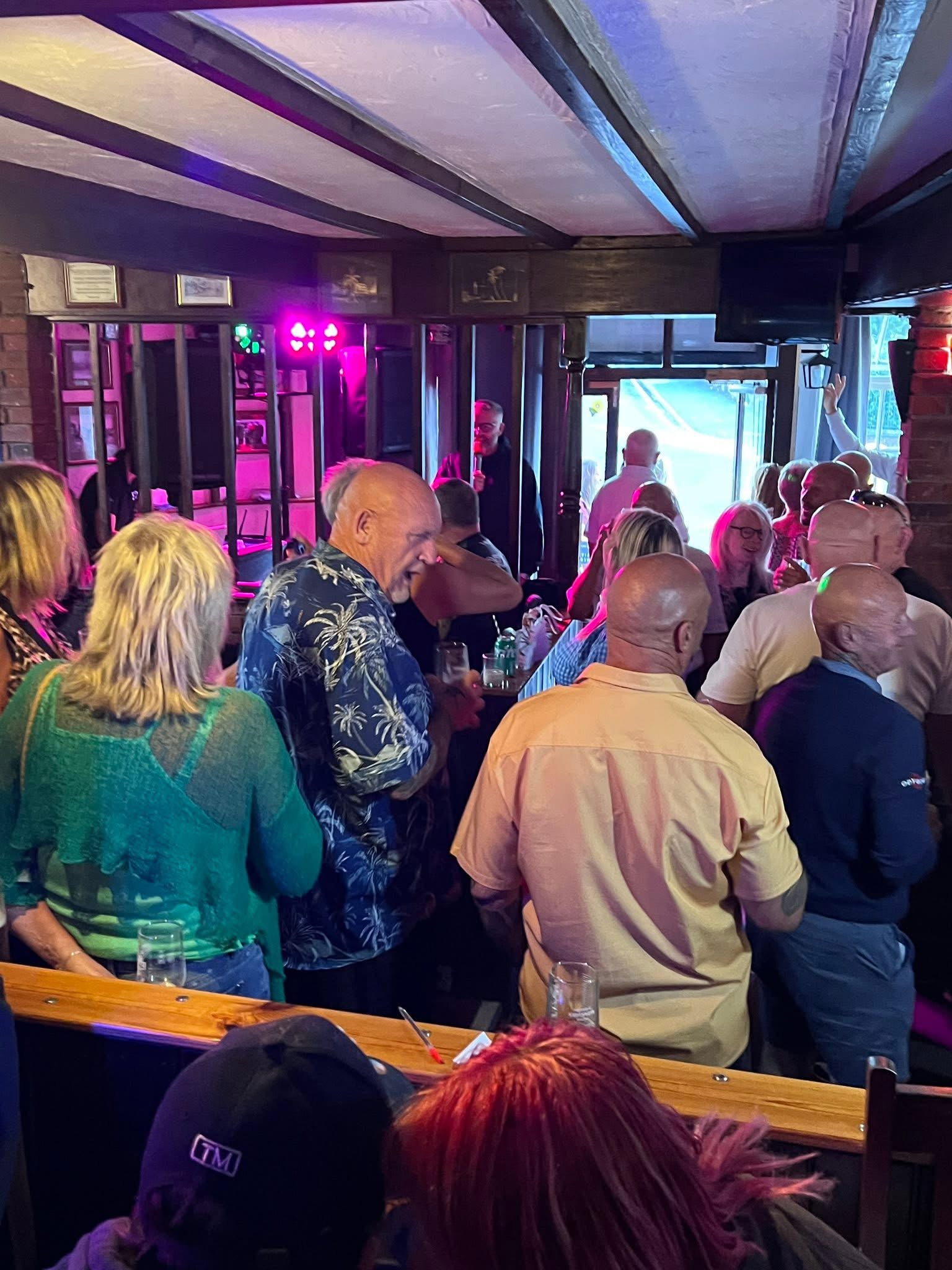 A busy pub crowd enjoying karaoke with coloured stage lights.