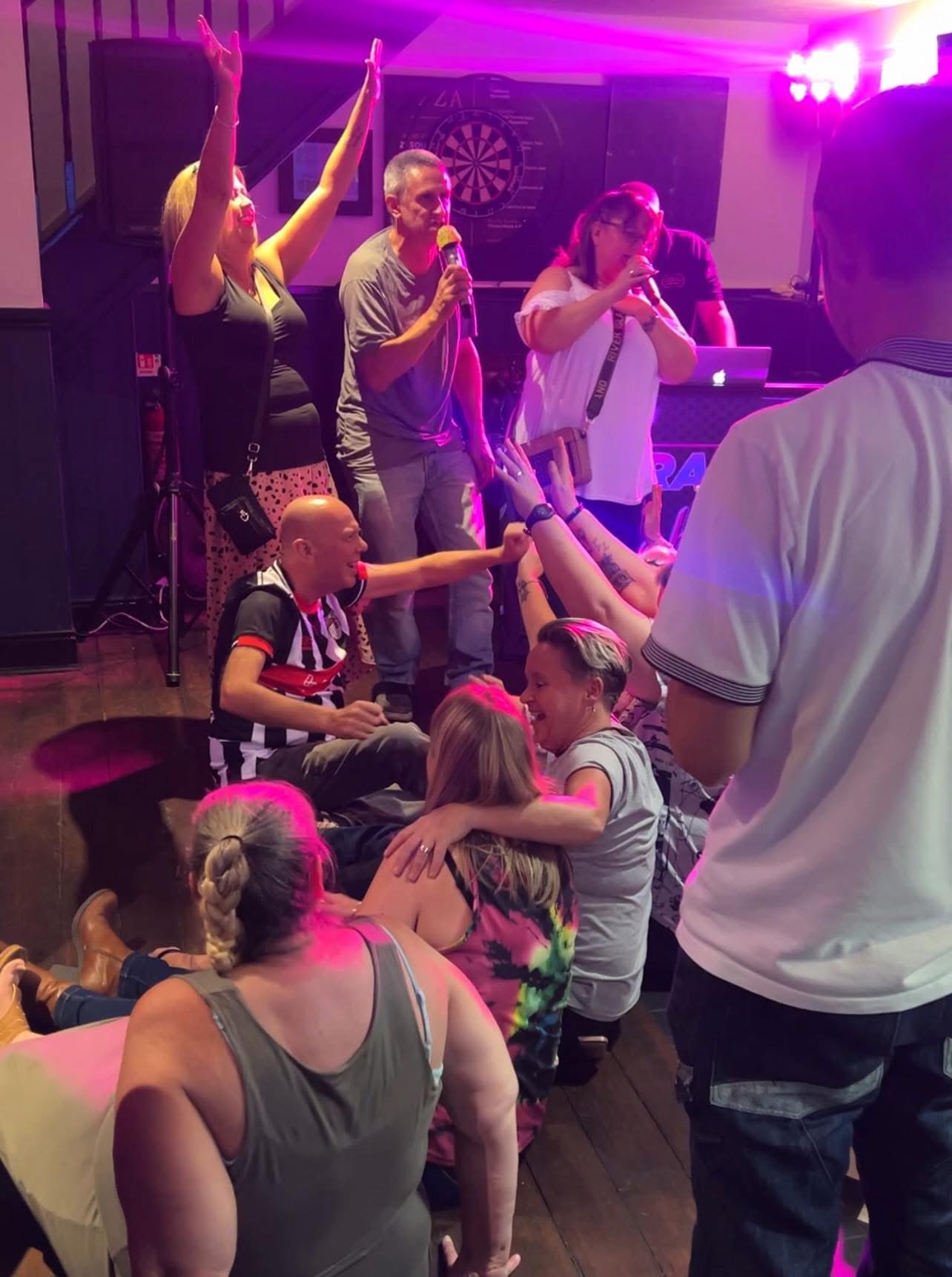 A group singing karaoke together in front of the hosting booth.